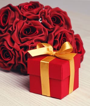 red roses and red gift box with yellow ribbon on wooden surface