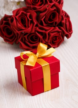 red roses and red gift box with yellow ribbon on wooden surface