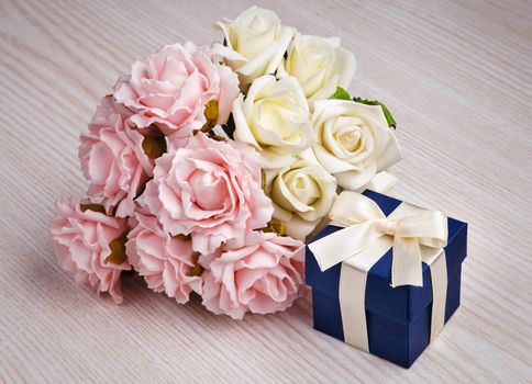 roses and blue gift box with white ribbon on wooden surface