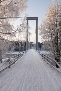 A bridge in a winter landscape with some sunlight on the birches