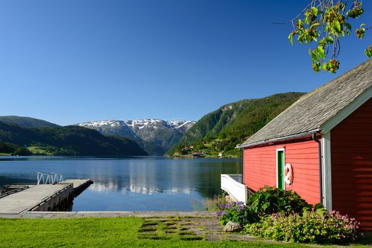 Fjord view over Hardangerfjord with a red boathouse (naust) and a small pier in Ulvik in Hordaland county, Norway.
