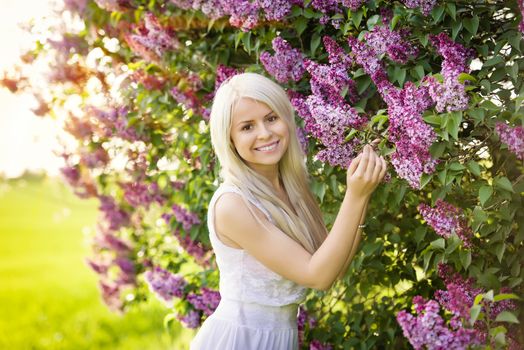 Beautiful smiling young blond woman in white dress with lilac flowers