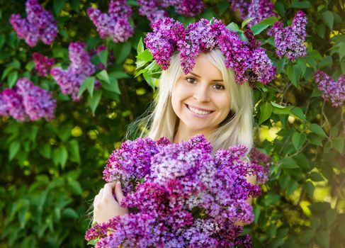 Beautiful smiling young woman is wearing wreath and bouquet of lilac flowers 