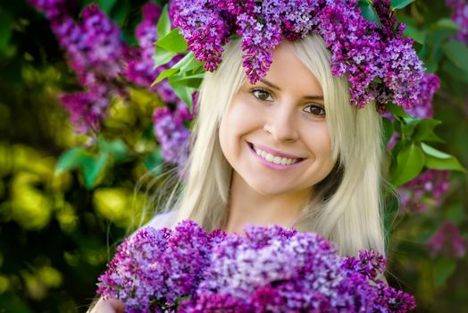 Close Up portrait beautiful smiling young blonde woman is wearing wreath of lilac flowers and bouquet