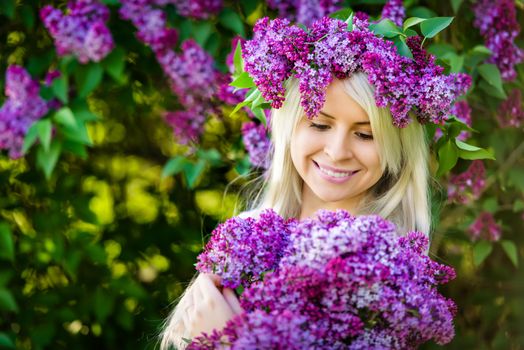 Beautiful smiling young woman is wearing wreath and bouquet of lilac flowers 