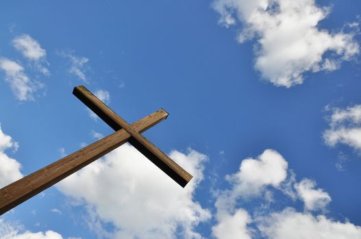 Wooden cross against blue sky with white clouds