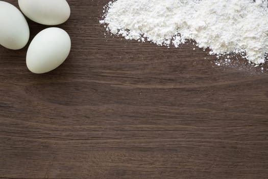 Top view of baking background with eggs and flour on vintage natural wood table. Rough texture and rustic surface with blank space for text.