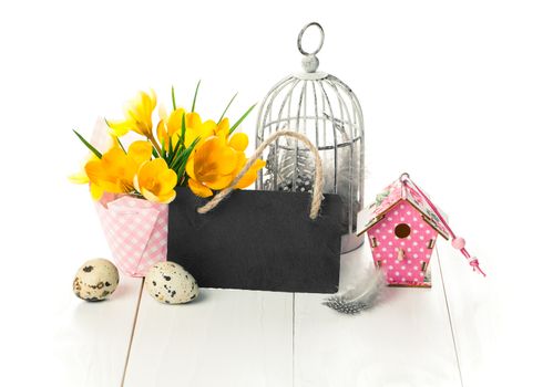 easter decoration with quail eggs, birdcage, yellow Spring Crocus, and blackboard, with space for text, on wooden white background.