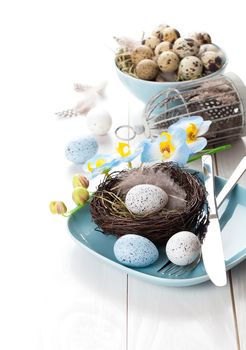 table decoration with easter eggs nest on plate, on white wooden background
