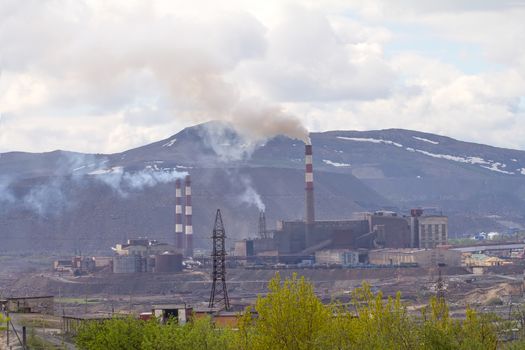 ore processing plant, from pipes coming out  smoke. In  background  waste rock dumps. 