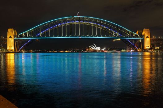 SYDNEY, AUSTRALIA - JUNE 3, 2013;  Sydney Harbour Bridge lit in blue and aqua colours and reflections in Sydney Harbour.  Sydney Opera House in far view.