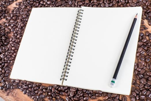 Pencil, notebook and coffee beans on wooden background