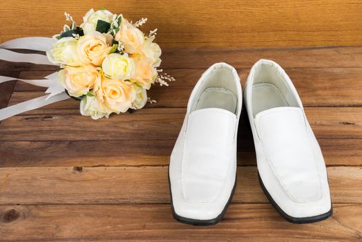 Wedding bouquet with groom's shoes on wood floor background