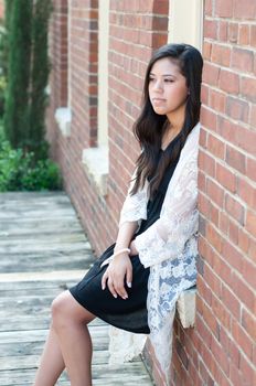 Outdoor shot of attractive teen wearing a dress and sitting in window of brick building.