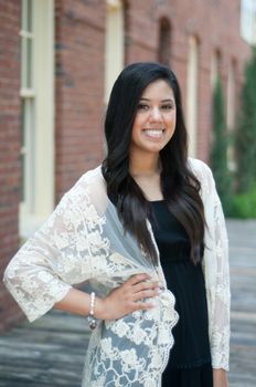 Beautiful and happy senior graduate standing in front of building wearing a dress.