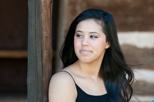 Beautiful teen girl looking to the side leaning on wood pole.