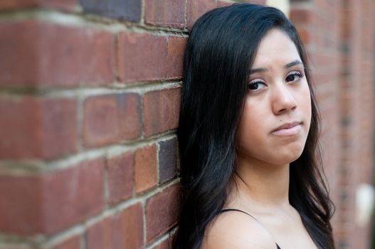 Beautiful and depressed teen girl leaning on a brick wall building.