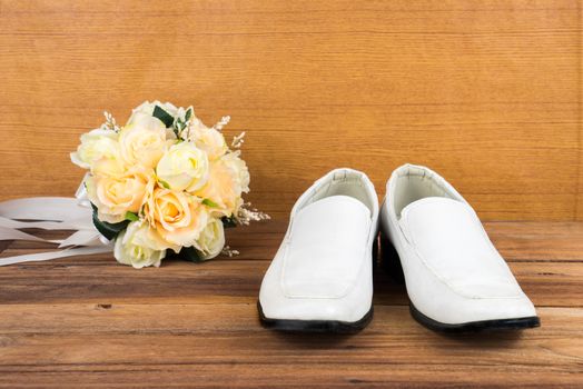 Wedding bouquet with groom's shoes on wood floor background