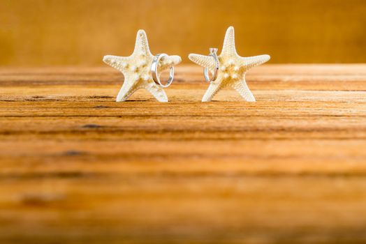 Two wedding rings with two starfish on wooden table, vintage wedding look with space for text