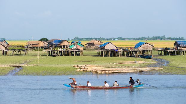 Sittwe, Rakhine State, Myanmar - October 16, 2014: Traditional boat passing a village along the Kaladan River at the Rakhine State in Myanmar.