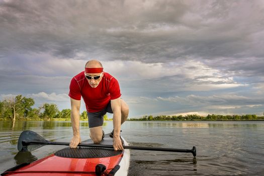 senior male paddler starting his workout on  stand up paddleboard, a local lake in Colorado under cloudy sky