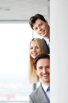 Happy business people looking out from corner in office