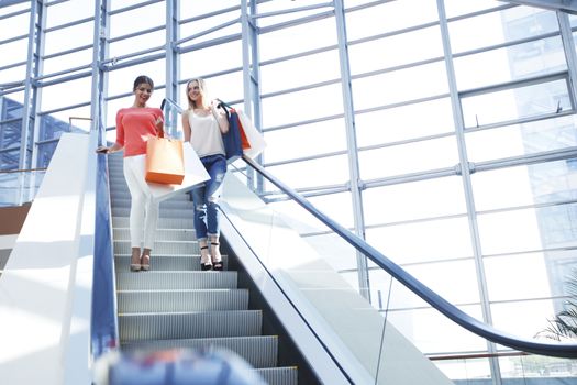 Young beautiful happy women on escalator of shopping mall