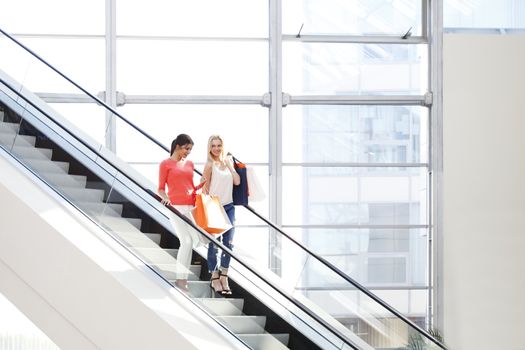 Young beautiful happy women on escalator of shopping mall