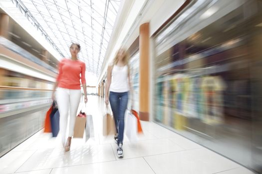 Women walking fast in shopping mall with bags