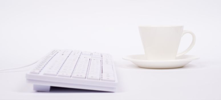 Computer keyboard and cup on isolated white background, side view