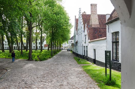 Bruges, Belgium - May 11, 2015: People visit White houses in the Beguinage (Begijnhof) in Bruges, Belgium. In 1937 the beguinage became a monastery for the Benedictine sisters who still live here now.