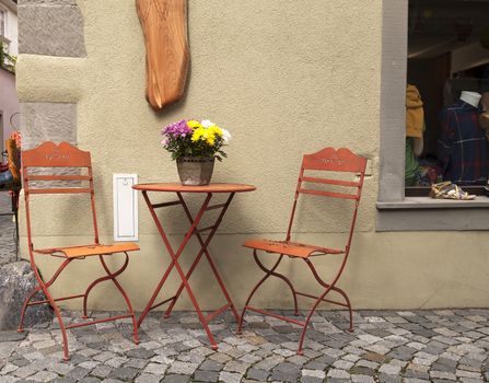 Two chairs and a table with a flower outside a shop