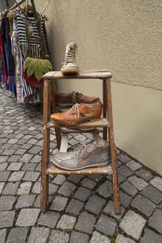 Shoes on a stool on a street with clothes in the background