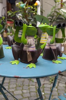 A set of frogs with binoculars on a table in front of a shop