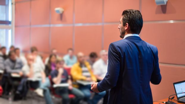 Speaker at Business Conference with Public Presentations. Audience at the conference hall. Entrepreneurship club. Rear view. Horisontal composition. Background blur.