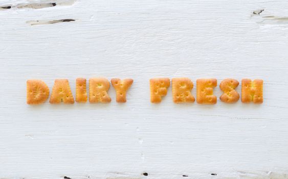 The character word DAIRY FRESH. Alphabet cookie crackers putting on rough surface of white wood background.