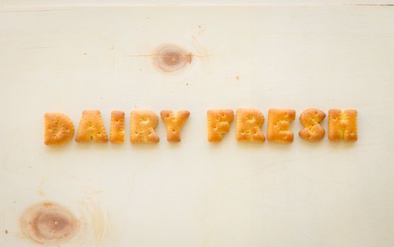 Close up the capital letters word DAIRY FRESH . Alphabet cookie biscuits putting on wood texture and background.