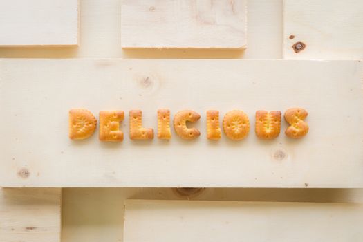 The capital letters word DELICIOUS. Alphabet cookie biscuits putting on piece of wood background.