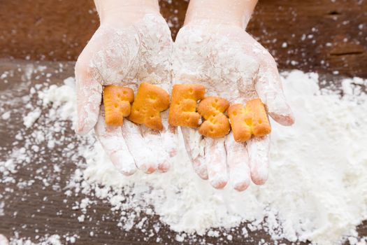 Close up the letters word FRESH alphabet cookie biscuits putting on kid hands with cooking flour.