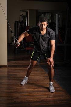 Handsome young african descent mixed race man doing one arm standing high cable fly workout in gym