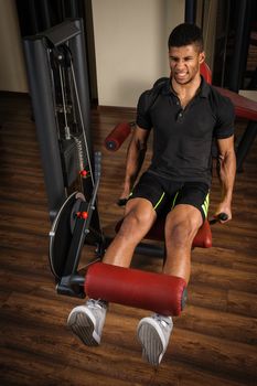 handsome young african descent mixed race man doing legs extensions workout in gym