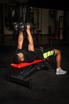 handsome young african descent mixed race man doing arms bench flies workout with dumbbells in gym