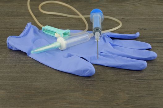 Disposable infusion set, syringe and glove placed on wooden table.                               