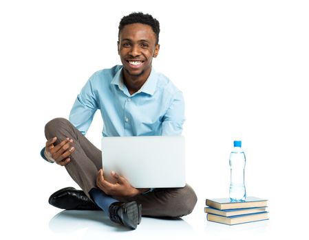 Happy african american college student with laptop, books and bottle of water sitting on white background