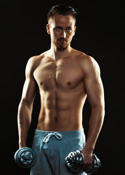 Athletic attractive man with dumbbells on the black background