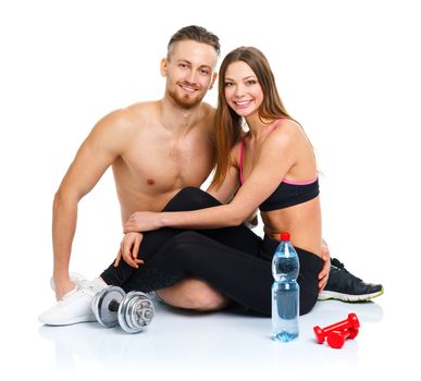 Athletic couple - man and woman after fitness exercise with dumbbells and bottle of water sitting on the white background