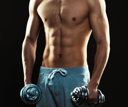 Athletic attractive man with dumbbells on the black background