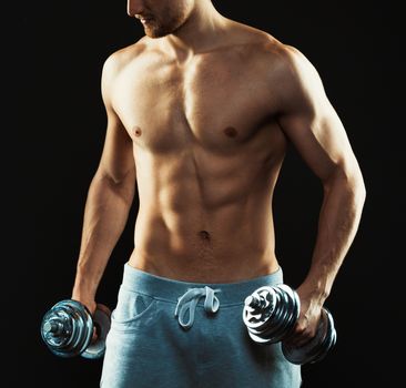 Athletic attractive man with dumbbells on the black background