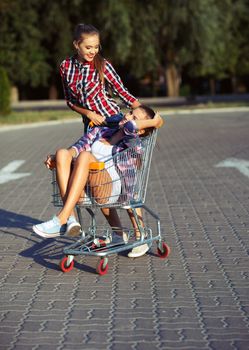 Two happy beautiful teen girls driving shopping cart outdoors, lifestyle concept