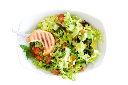 Fresh healthy plain Mediterranean salad with lettuce, peppers, tomato and black olives with a bitten toasted bun resting on top served in a white bowl, isolated on white
